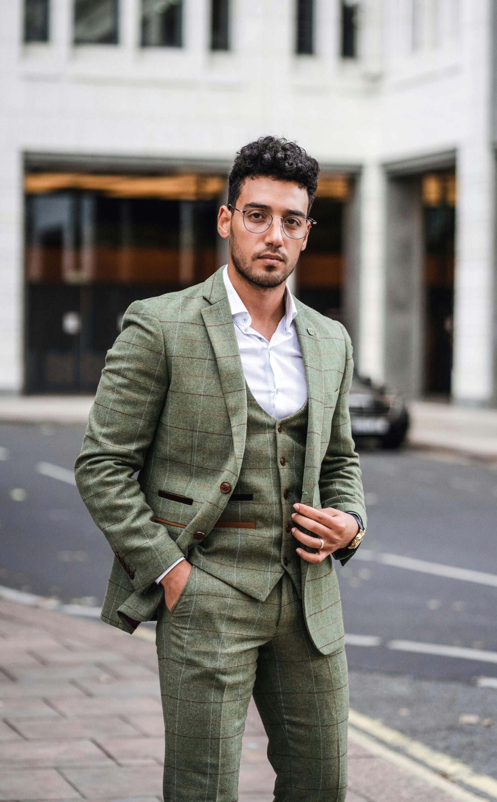 Elegant businessman in a green suit posing confidently on a city street with an urban background.