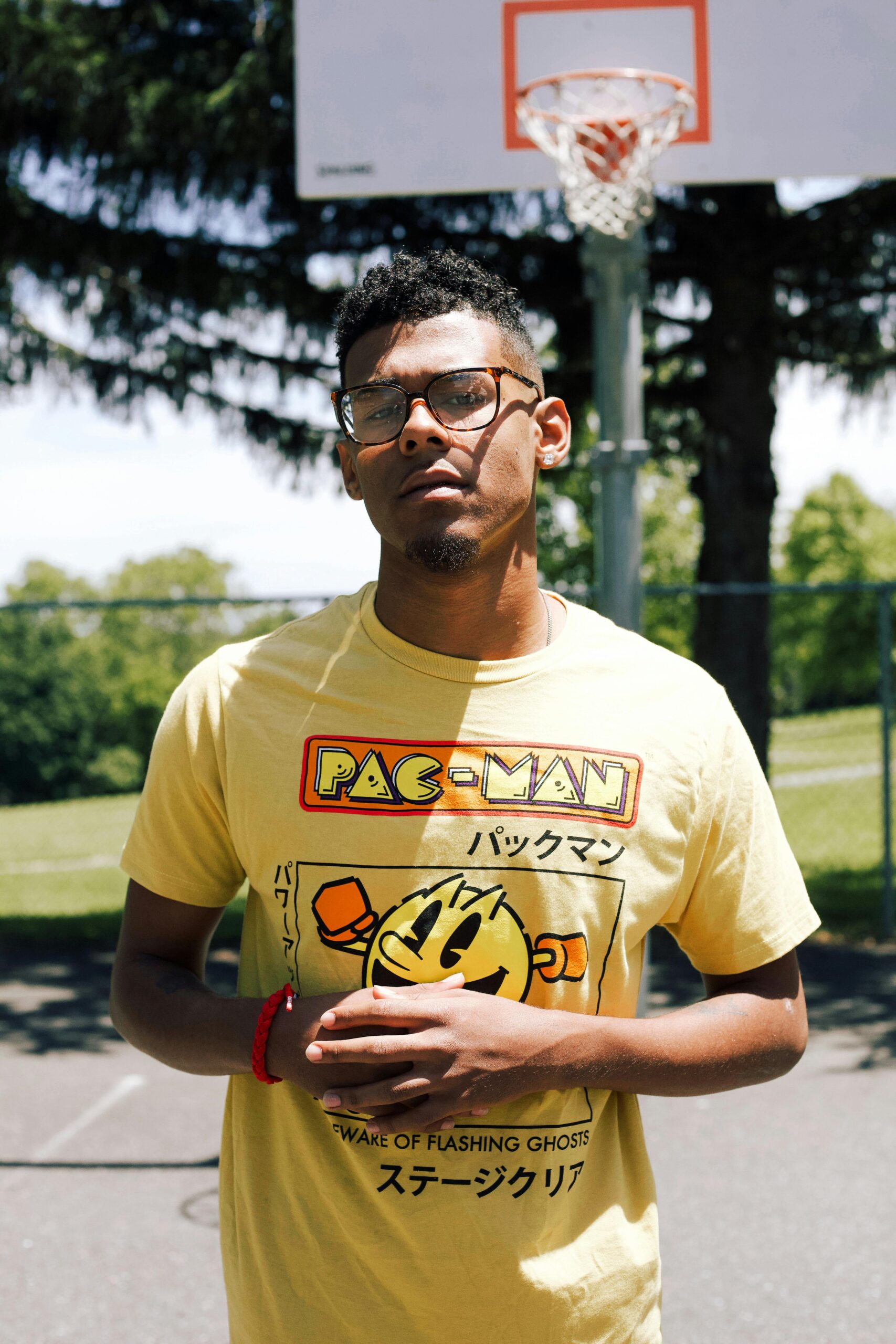 Adult man in a yellow t-shirt posing in front of a basketball hoop outdoors.